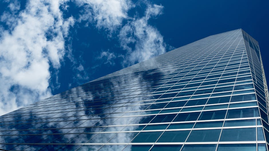 Low-angle view of a modern skyscraper with reflective glass windows against a blue sky.